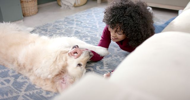 Young woman engaging in playful interaction with dog on living room floor, showcasing joy of pet companionship. Perfect for themes of pet care, relaxation at home, and human-animal bond. Great for marketing campaigns for pet products, home comfort, or lifestyle blogs.