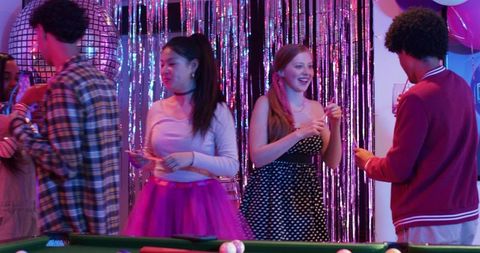 Multicultural friends celebrating neon disco pool party playing billiards in retro outfits