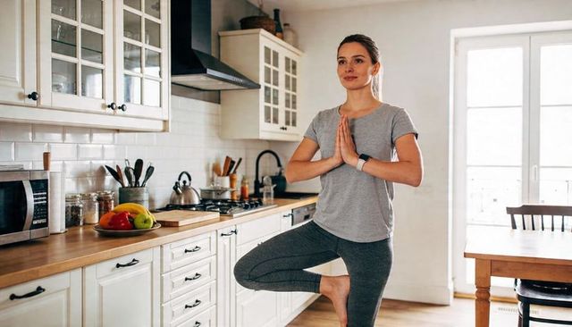 Woman practicing tree pose in bright kitchen wearing smartwatch promoting mindful living