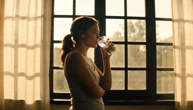 Woman drinking water by sunlit window in minimalist home interior morning ritual backlit silhouette