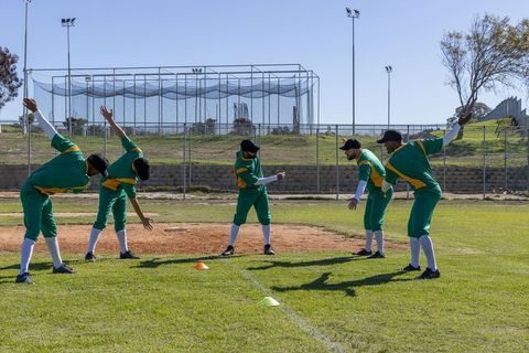 Diverse male baseball team warming up on grass field during training drill with cones