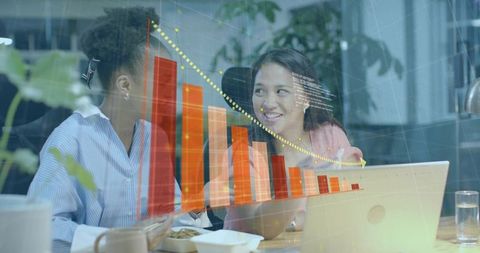 Women collaborating over laptop analyzing downward bar chart during office meeting together
