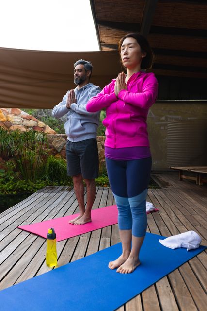 Diverse couple standing and practicing yoga in garden together. Spending quality time together at home concept.