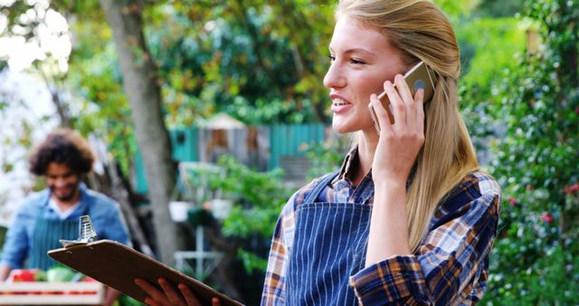 Female vendor talking on phone with clipboard outdoors - Download Free Stock Images Pikwizard.com