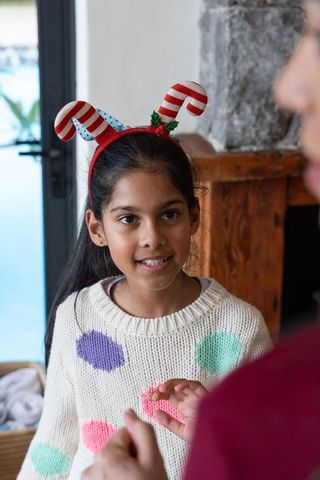 Indian preteen girl wearing candy cane antler headband and polka dot sweater celebrating holidays