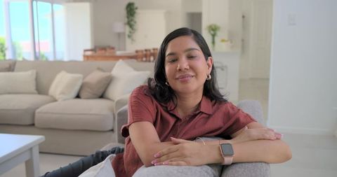 Relaxing woman leaning on sofa in contemporary open-plan living room, wearing smartwatch