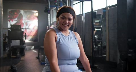 Mid-adult woman smiling while resting on bench in gym wearing light blue workout set