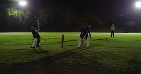 Night cricket match batsman holding bat at crease under stadium floodlights