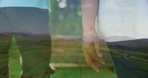 Senior couple standing hand over rolling green fields double exposure evoking connection