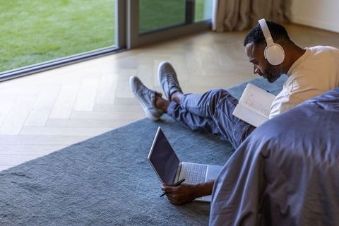 Mature african american man working from home on laptop with headphones and notebook