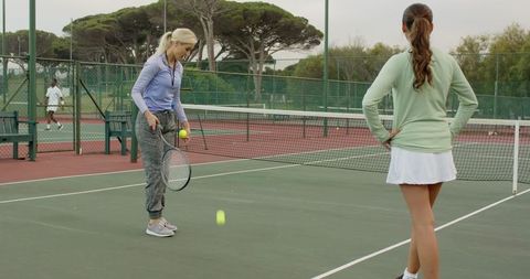 Women practicing tennis drills on outdoor court bouncing ball and racket training session