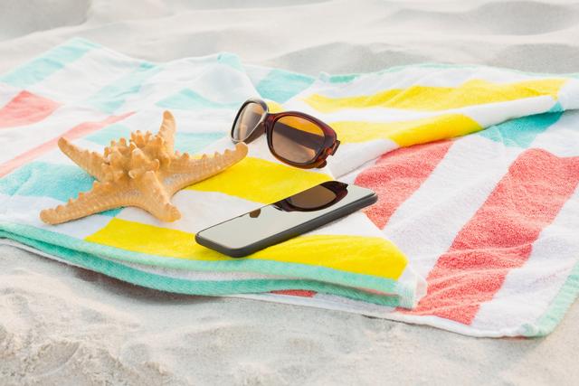 Starfish, sunglasses and mobile phone kept on beach blanket at beach