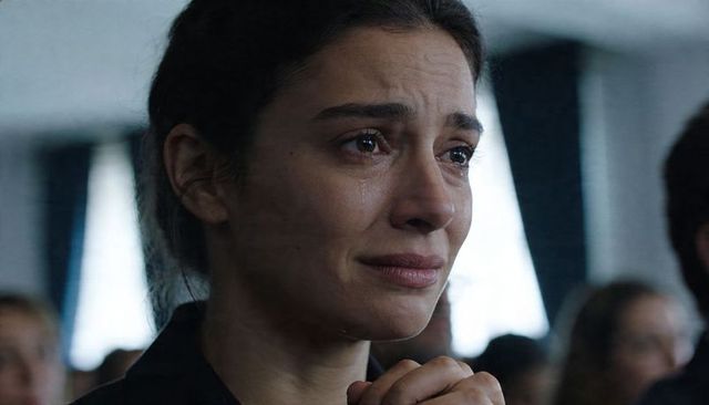 Crying woman clasping hands during memorial ceremony showing tear streaks and somber look