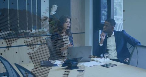 Executive colleagues discussing strategy in modern glass boardroom with laptop