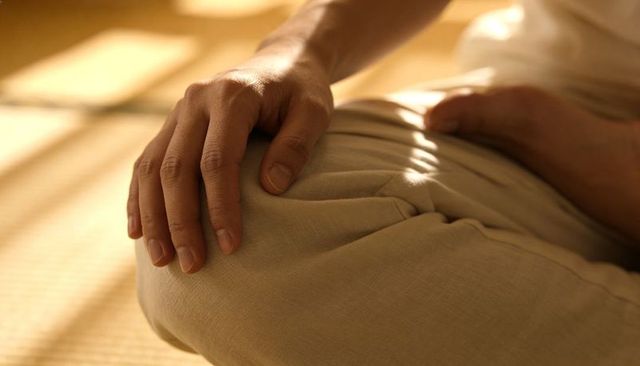 Resting hand on knee on tatami mat in warm sunlight, beige trousers, calm minimal moment