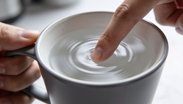Finger creating concentric ripples in water-filled gray ceramic mug close-up for mindfulness