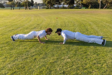 Cricket players doing push-ups facing each other on grass field during training