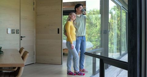 Young couple enjoying morning coffee by glass doors overlooking green deck and forest