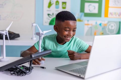 African american boy studying renewable energy with laptop and wind turbine models
