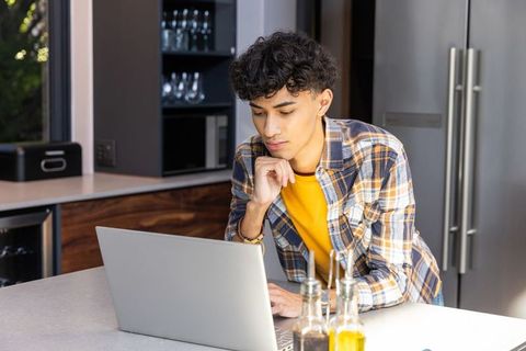 Asian man working on laptop in modern kitchen setting