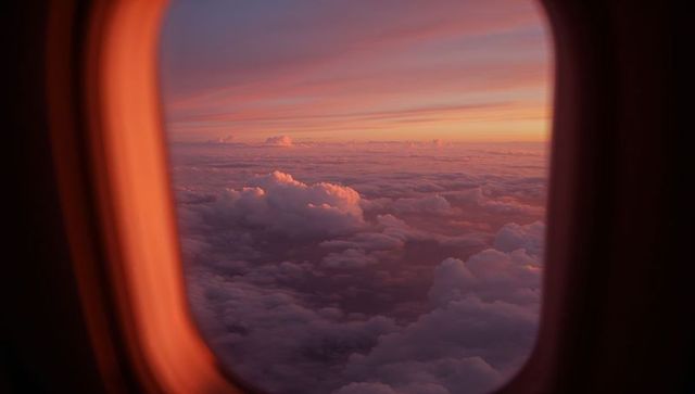Framing pastel sunrise over expansive cloudscape through airplane window rim