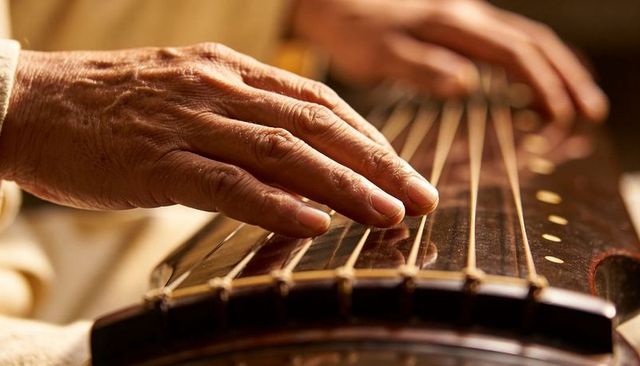 Senior hands plucking guzheng strings in warm amber light, traditional chinese music