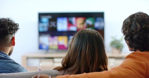 Three friends watching streaming tv on couch in cozy modern living room