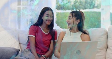 Smiling young women sharing laptop on sofa in bright natural light