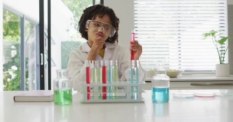 Young scientist experimenting with colorful test tubes on bright kitchen counter