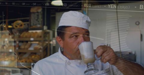 Mature baker sipping latte in artisan bakery with overlaid financial charts and warm light