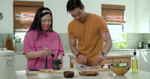 Couple cooking together grinding herbs and chopping vegetables on modern kitchen island