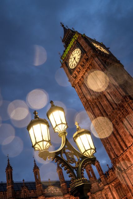 Iconic image of Big Ben clock tower illuminated at night, alongside a glowing street lamp in London. Ideal for use in travel promotions, tourism brochures, historical features, or posters depicting famous landmarks. The bokeh effect adds a dreamy quality perfect for artistic and inspirational content about urban landscapes.