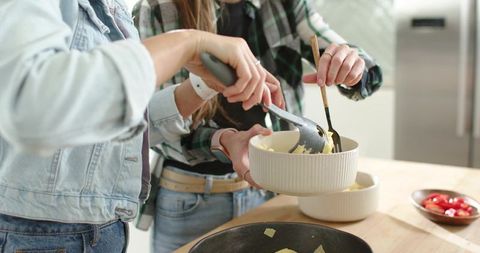 Friends preparing cozy potato meal together on wooden counter with ribbed ceramic bowls
