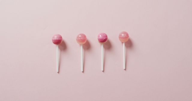 Four identical pink lollipops are evenly spaced in a row on a pastel pink background. This minimalist and aesthetically pleasing setup highlights the simple beauty of the sweet treats. Ideal for promoting candy shops, blogs about sweets, and as artistic decoration for events and parties.