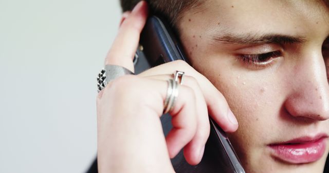 Young man intensely engaged in conversation using a smartphone. This image can be used to depict themes of communication, modern technology, personal conversation, youth, and expression of emotion. Suitable for advertisements, blogs, or articles discussing mobile technology, personal relationships, or lifestyle.