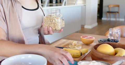 Woman preparing healthy breakfast with oats, banana and grapefruit in cozy sunlit kitchen