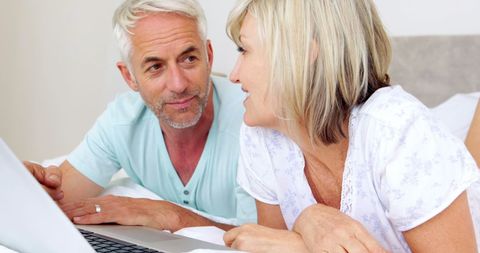 Happy Mature Couple Relaxing with Laptop in Bedroom