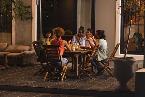 Friends dining on patio under candlelight and string lights, evening outdoor gathering