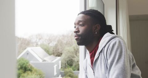 Contemplative African American Man Leaning on Window Ledge Looking Out Over Quiet Suburban Homes