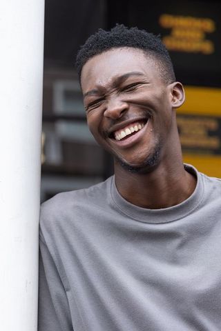African man laughing and smiling with eyes closed leaning on white post, candid urban headshot