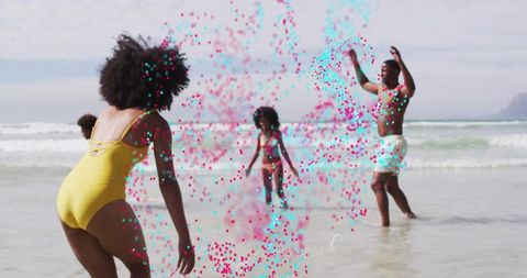 Family playing on beach tossing pink and teal powder confetti along sunny shoreline