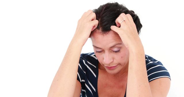 A middle-aged Caucasian woman appears stressed or upset, clutching her head with both hands, with copy space. Her expression and body language suggest worry, frustration, or a headache.