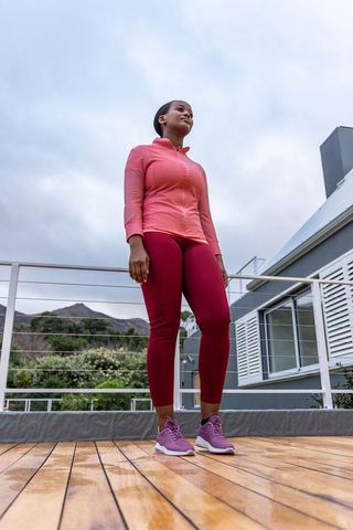 Confident african american woman standing on rooftop deck in pink activewear