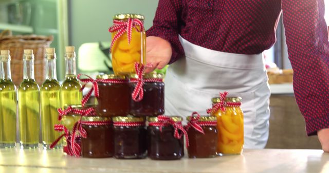 Person arranging jars of homemade fruit preserves and jams neatly on kitchen surface. Perfect for stories about homemade food, canning, preserving fruits, and preparing homemade goodies. Could be useful in articles, blogs, and articles focused on homemade cooking and recipes.
