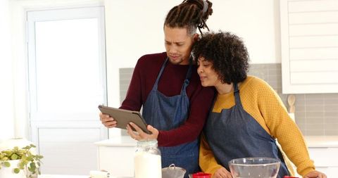 Couple baking together in sunlit kitchen consulting tablet for recipe inspiration