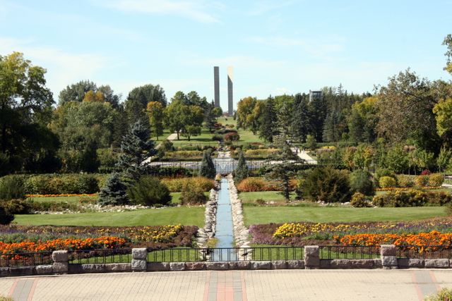 Peaceful garden scene featuring well-manicured flower beds, lush greenery, and a prominent monument visible in the background under a clear blue sky. Ideal for illustrating concepts of tranquility, nature, and outdoor beauty, suitable for promoting parks, relaxation, and environment-focused content, or for use in travel brochures and garden design inspiration.