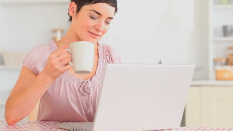 Woman Relaxing with Tea While Using Laptop in Kitchen