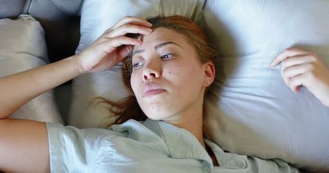Pensive woman lying on pillow touching forehead, resting in bed wearing loungewear