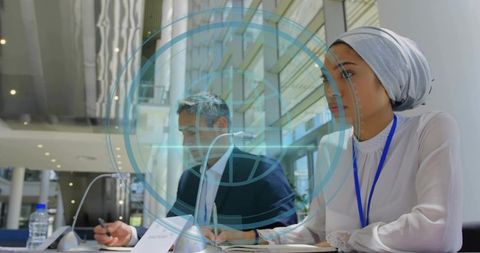 Business conference with woman wearing headscarf taking notes in modern glass atrium
