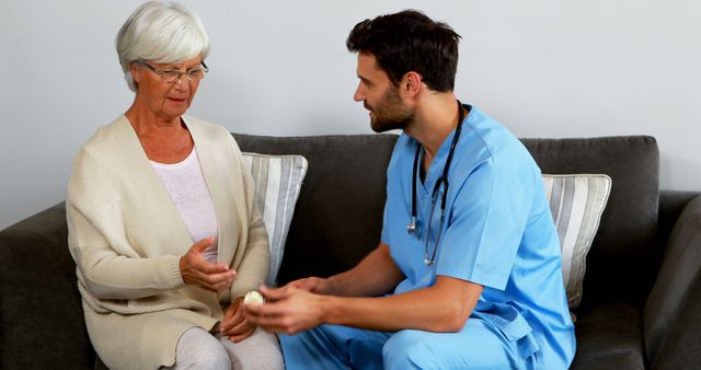 A senior Caucasian woman is having a consultation with a young Caucasian male nurse, both engaging in a conversation. It illustrates a healthcare professional providing support and advice to an elderly patient, emphasizing the importance of patient-centered care.
